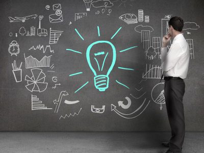 Businessman looking at drawings on a wall with a light bulb and different charts
