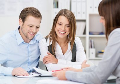 Investment adviser giving a presentation to a friendly smiling young couple seated at her desk in the office