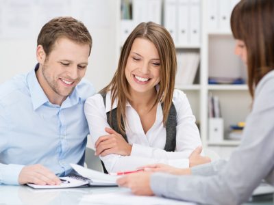 Investment adviser giving a presentation to a friendly smiling young couple seated at her desk in the office